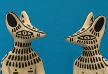 Two biege sculptures featuring what appears as dogs with black painted markings on blue background