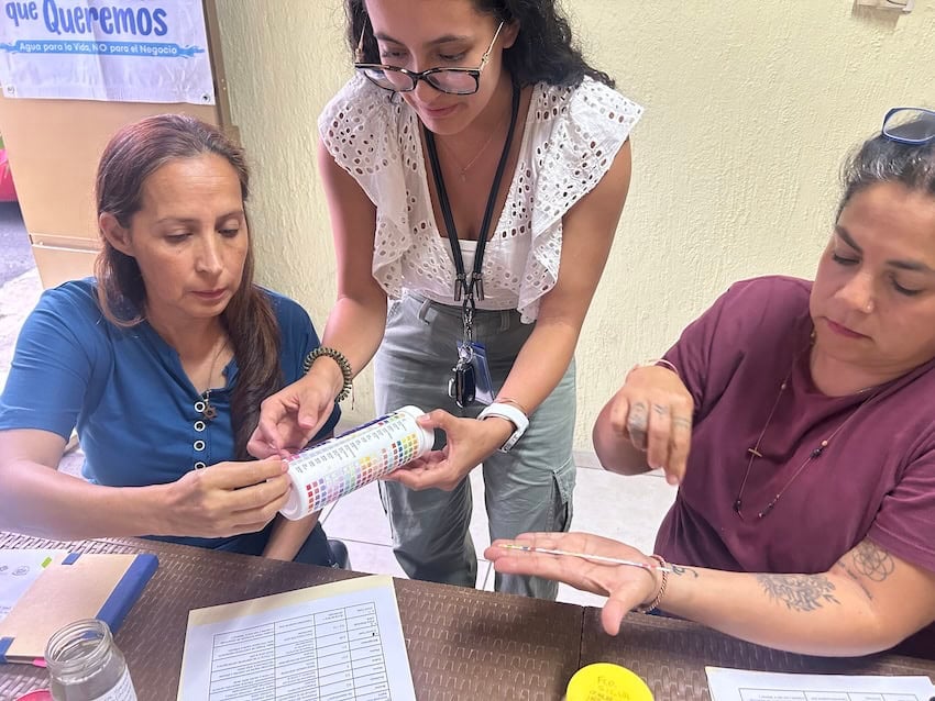 An environmental engineer helps residents compare the colors on test strips dipped in water from their home taps with a reference chart.