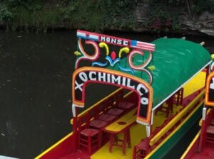 a colourful sign displays "Xochimilco" on a small barge on a small creek