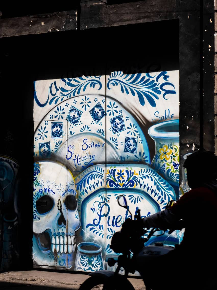 Man on bike passing Dia de Muertos art in Puebla. 