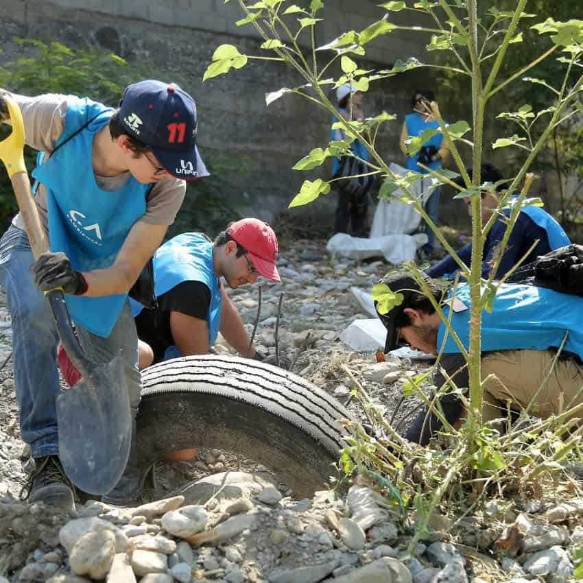 Several boys in blue bibs planting and digging on a riverbed in Monterrey, beside trash