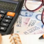 mexican pesos with a calculator and a pair of glasses on a table