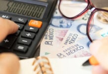 mexican pesos with a calculator and a pair of glasses on a table