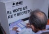 A man votes at a booth reading INE: El voto es libre y secreto