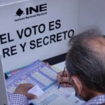 A man votes at a booth reading INE: El voto es libre y secreto