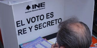 A man votes at a booth reading INE: El voto es libre y secreto