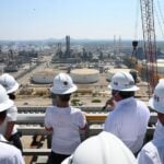 Group of authorities and Sheinbaum in hard hats looking out at Pemex facilities