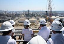 Group of authorities and Sheinbaum in hard hats looking out at Pemex facilities