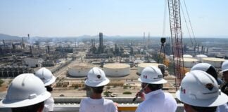 Group of authorities and Sheinbaum in hard hats looking out at Pemex facilities
