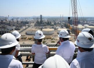 Group of authorities and Sheinbaum in hard hats looking out at Pemex facilities