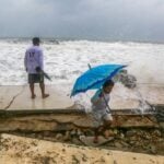 two people duck from splattering ocean water as a hurricane approaches Mexico