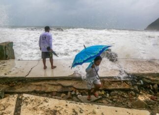 two people duck from splattering ocean water as a hurricane approaches Mexico