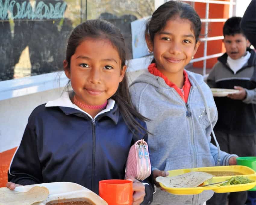 Two girls who have hot meals on trays courtesy of Feed the Hungry San Miguel