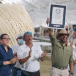 A man holds up a Guiness World Record plaque in front of a giant ball of quesillo string cheese