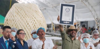 A man holds up a Guiness World Record plaque in front of a giant ball of quesillo string cheese