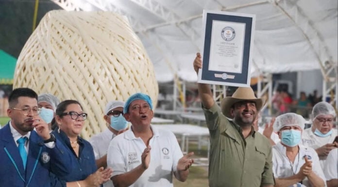 A man holds up a Guiness World Record plaque in front of a giant ball of quesillo string cheese