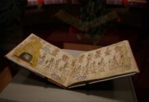 The yellowed pages of the Azcatitlan Codex, showing illustrations of Indigenous people in a line under a pyramid and columns bearing a variety of symbols