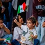 a young boy waving a mexican flag standing in front of a group of girls
