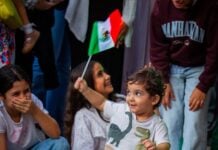 a young boy waving a mexican flag standing in front of a group of girls
