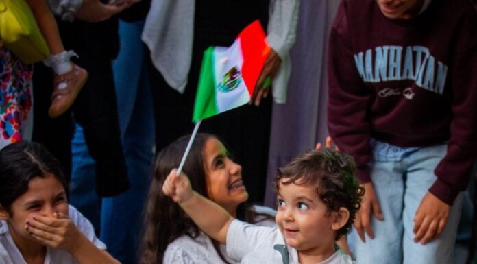 a young boy waving a mexican flag standing in front of a group of girls