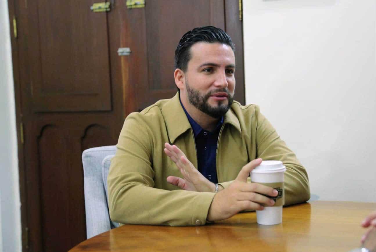 a man wearing a gold jacket drinking a coffee and listening to someone.