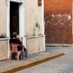 Man sitting in a red plastic Coca-Cola chair on the street