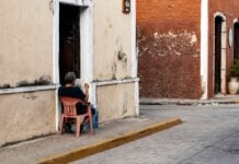 Man sitting in a red plastic Coca-Cola chair on the street