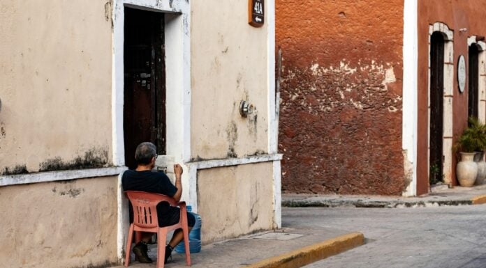 Man sitting in a red plastic Coca-Cola chair on the street