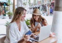 young latin women friends using laptop to shopping with credit card at restaurant at beach in Mexico Latin America, hispanic female in caribbean city with tropical weather.