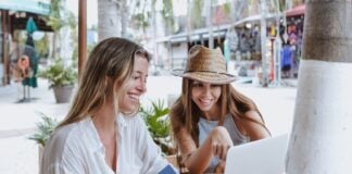 young latin women friends using laptop to shopping with credit card at restaurant at beach in Mexico Latin America, hispanic female in caribbean city with tropical weather.