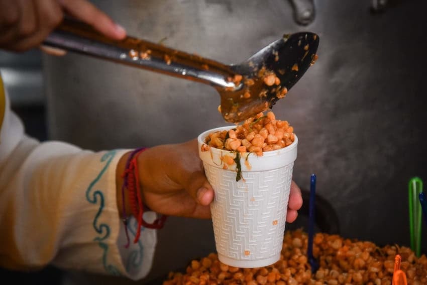 A hand pours corn kernals (with spices etc) into a white plastic cup to serve.