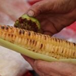 A man rubs his corn on the cob with lime and seasoning.