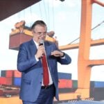 Ebrard standing in front of a presentation featuring an image of shipping containers
