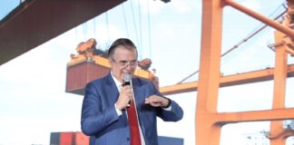 Ebrard standing in front of a presentation featuring an image of shipping containers