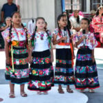 Four young girls in traditional Indigenous clothing hold microphones and speak at a Guerrero school