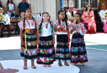 Four young girls in traditional Indigenous clothing hold microphones and speak at a Guerrero school