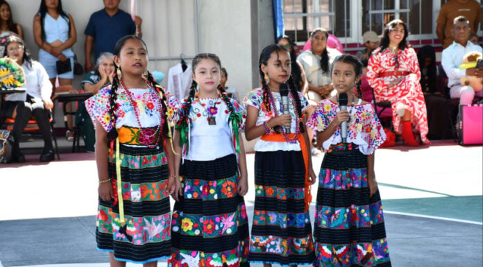 Four young girls in traditional Indigenous clothing hold microphones and speak at a Guerrero school