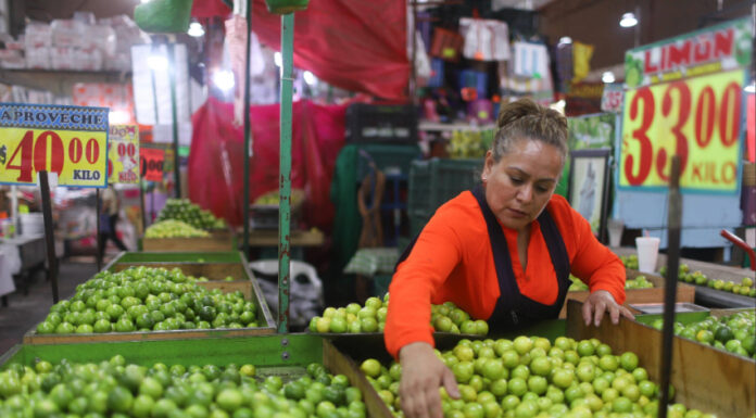 A woman arranges limes at a Mexican market display with price signs