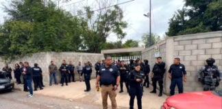 Police, emergency services and Civil Protection outside the cinder block fence and entrance of a school