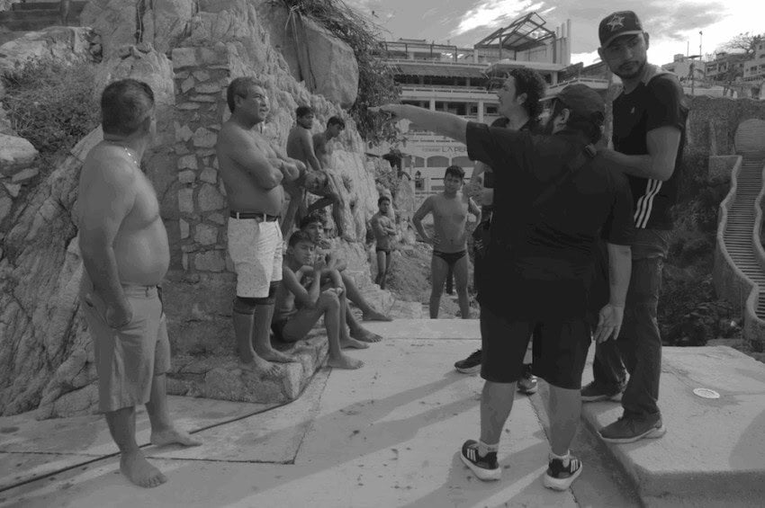 A group of men, topless clliff divers, getting direction from the film's directors.