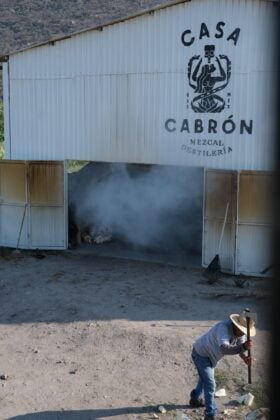 A man chopping something in front of the traditional mezcal palenque.