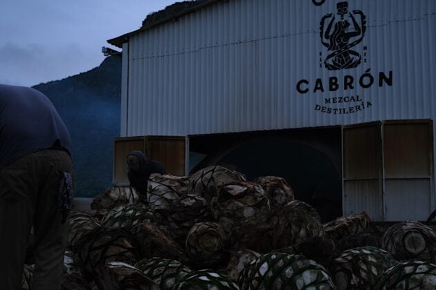 A palenque worker walks past the smoked shells of the agave plant.