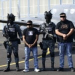 Mexican security forces stand with two men in handcuffs
