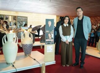 Two designers stand next to their artworks in a gallery.