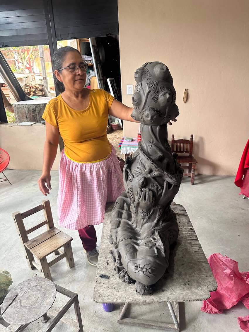 A woman in yellow t-shirt wokring ona. sculpture, appears grey. She is in her studio.