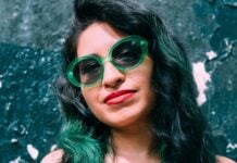 Young Hispanic woman with green hair tints and wearing green glasses.