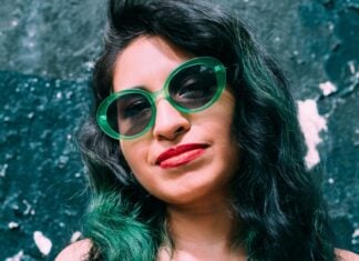 Young Hispanic woman with green hair tints and wearing green glasses.