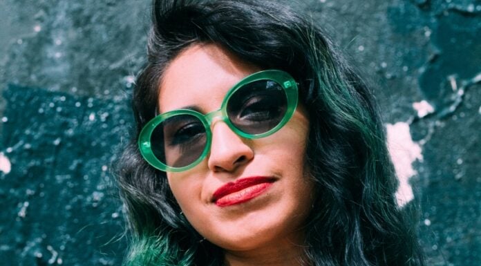 Young Hispanic woman with green hair tints and wearing green glasses.