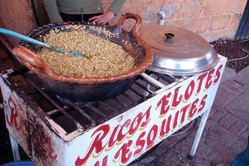 Someone stirring a big clay pot full of corn kernals, with the sign saying something like "delicious corn"