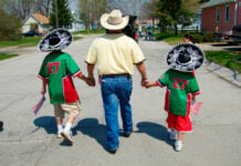 A family celebrates Cinco de Mayo in Port Huron, Michigan. A man in a cowboy hat holds the hands of two young boys in mariachi sombreros, holding US flags